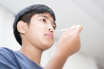 Asian boy self collecting nose swab for corona virus sample.Covid-19 laboratory test.Antigen test kit for rapid nose swab.Nasal swab is a test that takes a sample of cells from the nasopharynx.
