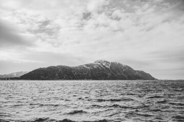 Shutter island style black and white picture. Island with snow capped mountain in the north sea. Scandinavia Norway Alesund.
