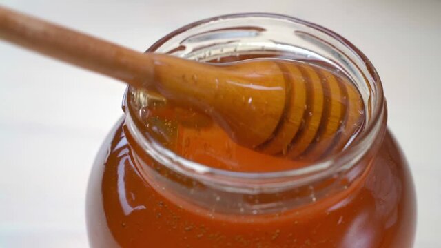 Wooden spoon mixes honey in the jar. Golden organic honey dripping in a bowl with a wooden stick closeup. Concept of healthy nutrition organic food. Background for beekeepers, healthy food stores