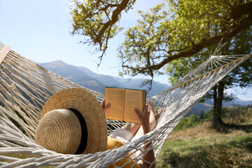 Young woman reading book in hammock outdoors on sunny day