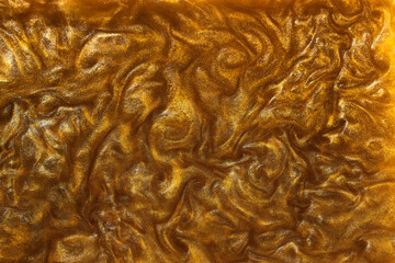 The texture of liquid gold with the addition of shiny pigment. Abstract golden texture of waves, swirls. Golden liquid acrylic paints. Modern design element.