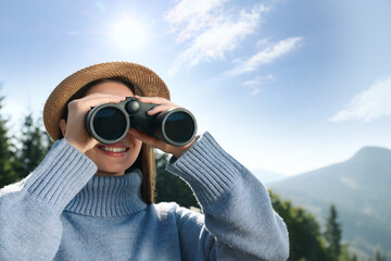 Fototapeta premium Young woman with binoculars in mountains on sunny day