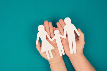 Parents with one child holding hands, paper cut out, copy space, petrol colored background, relationship