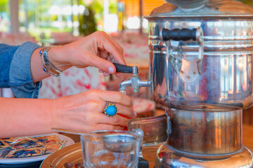 Traditional drinks concept - Samovar and Turkish tea enjoyment at picnic. Woman's hand pouring tea from samovar into glass. 