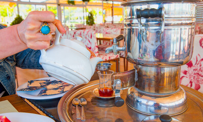 Traditional drinks concept - Samovar and Turkish tea enjoyment at picnic. Woman's hand pouring tea from samovar into glass. 