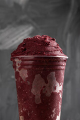 Brazilian Frozen Açai Berry Ice Cream Smoothie in plastic cup. On a wooden desk and a gray summer...