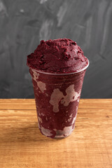 Brazilian Frozen Açai Berry Ice Cream Smoothie in plastic cup. On a wooden desk and a gray summer background. Front view for menu and social media