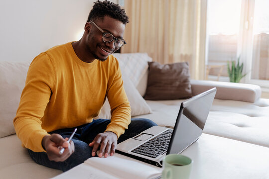 Cropped Shot Of A Handsome Young Businessman Sitting Alone In His Home Office And Working On Laptop Computer At Home. Smiling Black Man Using Laptop In Living Room. Businessman Using Laptop At Home.