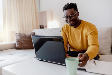 Photo series of African-American businessman at his home office taking a coffee break, while working on computer. Shot of handsome young black man happily working on his laptop at home during the day.