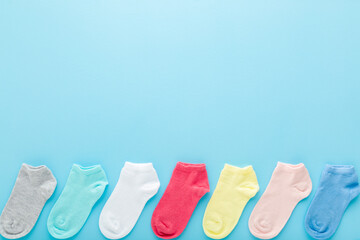 Row of colorful kid short socks on light blue table background. Pastel color. Closeup. Empty place for text. Top down view.