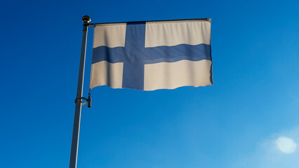 White flag of Finland with big blue cross in front of blue sky with lens flare. Diplomacy concept.