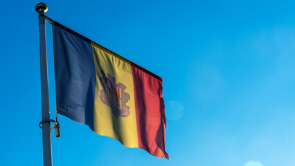 National flag of Andorra on a flagpole in front of blue sky with sun rays and lens flare. Diplomacy concept.