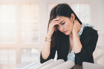 Young asian woman architect holding forehead and neck while working on project at office desk. She is tired and tired.