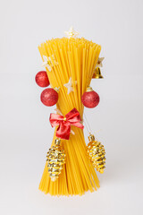 A bouquet of raw spaghetti in the shape of a Christmas tree with toys, red balls and pine cones.