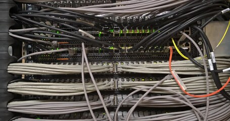 large number of wires and cables in modern server and network equipment with flashing green lights and optical severs computer in rack at data center