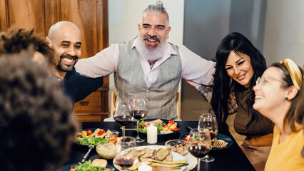 Adult cheerful friends hug happily, sitting at the table during a dinner