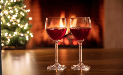 Two red wine glasses, burning fireplace background. Christmas tree bokeh lights decoration