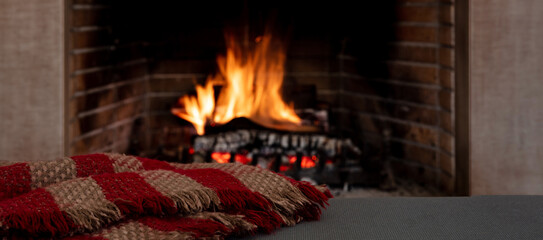 Blanket on fireplace burning wood logs background. Relaxation and Christmas holiday, cozy warm home