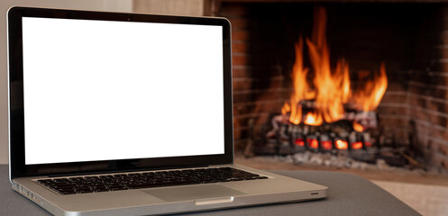 Christmas winter home office concept. Blank screen laptop on burning fireplace background,