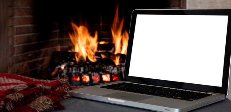 Christmas winter home office concept. Blank screen laptop on burning fireplace background, - Powered by Adobe
