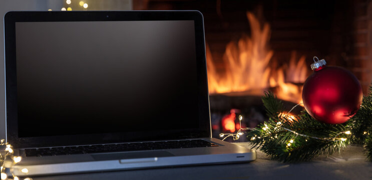 Christmas home office concept. Blank screen laptop on burning fireplace background. Winter holidays