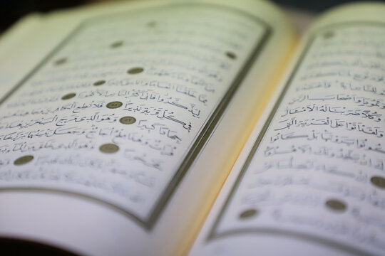 open quran pages. include arabic letters. selective focus on verse