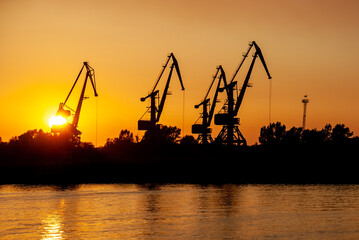 Obraz premium Silhouettes of tower cranes against the background of a sunset red sky.