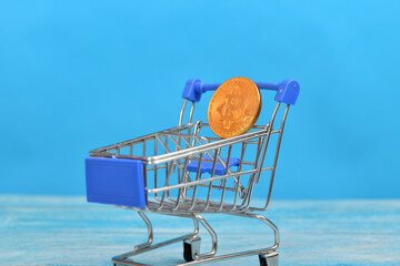Bitcoin coin in a consumer shopping cart on a blue background. coin in a consumer shopping cart.