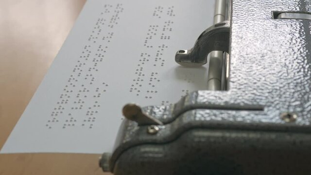 Close-up handheld shot of vintage braille typewriter machine writing Braille alphabets character encoding on paper .