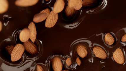 Closeup of falling almonds into dark melted chocolate