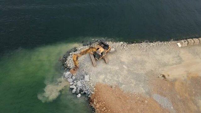 Aerial video. View from abobe and excavator working on building a land in a sea. Filling the shore with a stone. Coastline Strengthening, Erosion Control,Fighting the ocean Level Rise. Coastal