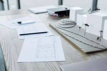 house models and blueprints near blurred notebooks and smartphone on wooden desk