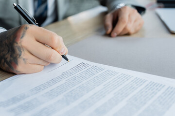 partial view of tattooed businessman signing blurred contract in office