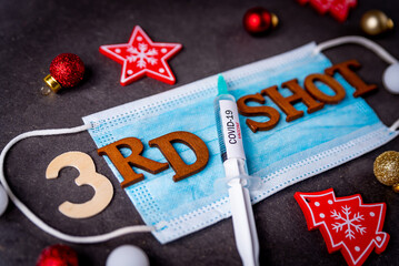 Third covid vaccine dose and jab concept with face mask and Christmas decorations. Syringe is seen...