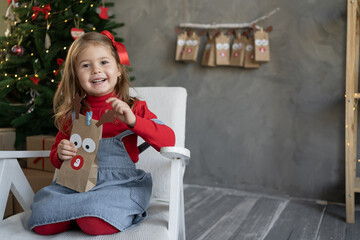 Gift concept for Christmas. Happy little girl with a package of advent calendar sitting at home on...