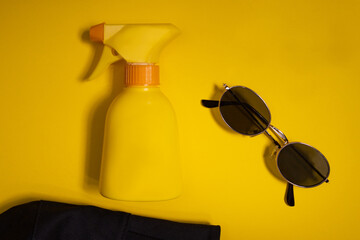 Yellow plastic small bottle on yellow background with dispenser, sunglasses and a cap 