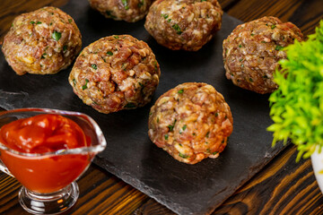 Fresh fried meatballs in the oven under tomato sauce. Tasty cheesy casserole. Raw ground meat. Homemade delicious food. Close up food on wooden background