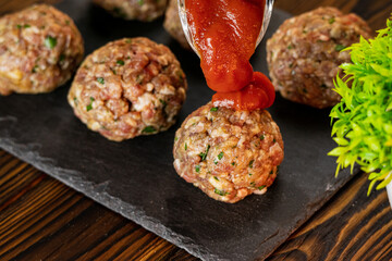 Fresh fried meatballs in the oven under tomato sauce. Tasty cheesy casserole. Raw ground meat. Homemade delicious food. Close up food on wooden background
