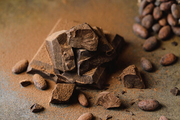 Pieces of dark chocolate with cocoa beans on brown background. 