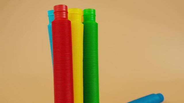 Group of multicolored rainbow toy pop it tube falls and rolls on beige background, trend toy for the development of fine motor skills of hands, anti stress crackling tube.