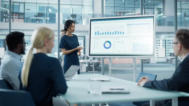 Female Operations Manager Holds Meeting Presentation for a Team of Economists. Asian Woman Uses Digital Whiteboard with Growth Analysis, Charts, Statistics and Data. People Work in Business Office.