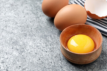 Raw chicken eggs and bowl with yolk on grey table, closeup, space for text