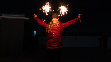 joven mujer con luces de bengala navideñas en la mano vestida con chamarra roja y gorro