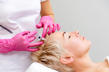 Professional beautician doctor in pink medical gloves holding filler syringe making injection to forehead. Anti-aging treatment and mesotherapy in cosmetology clinic