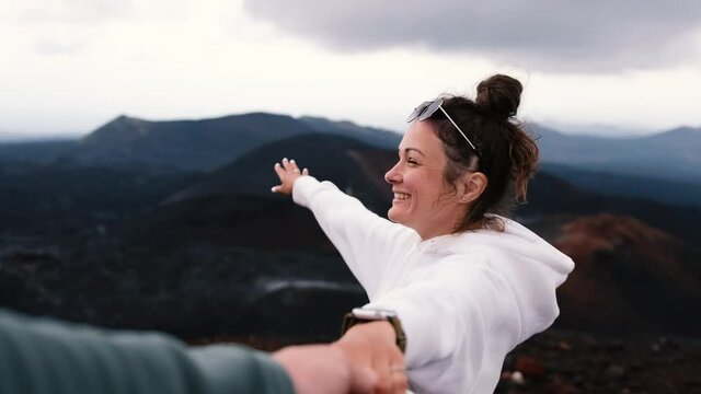 Young couple holding hands, woman leading boyfriend shows view of volcanoes
