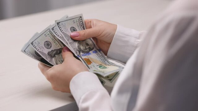 Female hands with dollar bills with an elastic band. American dollar bills wrapped by rubber band. Businesswoman hands recounting american paper currency 100 dollar banknotes. Save money. Dirty money