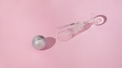 Champagne glass with silver metallic shiny bauble coming out of it.Christmas winter holidays aesthetic design on a pink background