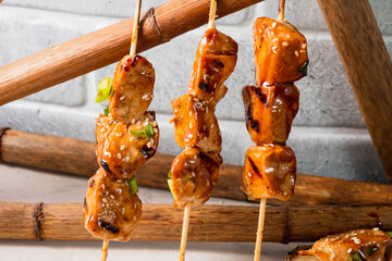 Delicious chicken skewers sprinkled with sesame seeds and green onions, three skewers stand upright.
