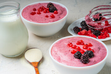 Two bowls with semolina mousse with red currants and blackberries. Milk, white background, spoon with semolina.