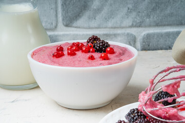 Mousse of semolina and red currant berries in a white bowl against a gray wall. Vegan dessert....
